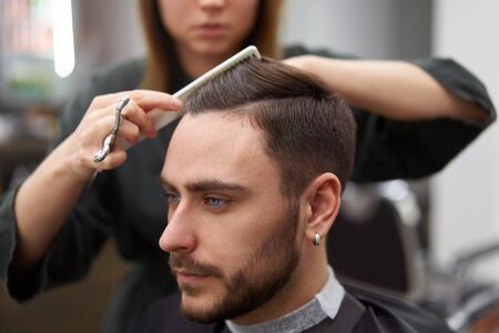 Stylish man sitting barber shop Hairstylist Hairdresser Woman cutting his hair Portrait handsome happy young bearded caucasian guy getting trendy haircut Attractive barber girl working serving client の写真素材