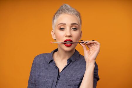 Close up portrait makeup artist. Make up courses. Concept of self visage masterclasess. Fashion professional. Woman hold makeup brushes on the hands. Studio shot on the orange color backgroundの写真素材
