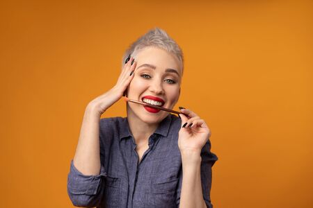 Close up portrait makeup artist. Make up courses. Concept of self visage masterclasess. Fashion professional. Woman hold makeup brushes on the hands. Studio shot on the orange color backgroundの写真素材