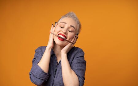 Close up portrait makeup artist. Make up courses. Concept of self visage masterclasess. Fashion professional. Woman hold makeup brushes on the hands. Studio shot on the orange color backgroundの写真素材