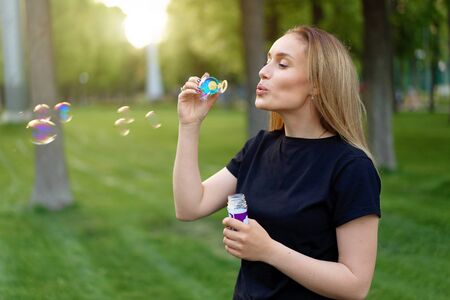 Young beautiful girl blowing soap bubbles in the summer sunny park Summertime leisure. Positive and happy people.の写真素材