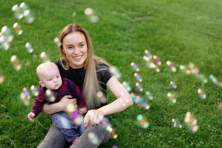 Young Caucasian mother inflates soap bubbles with her little son in a park on a sunny summer day. happy family leisureの写真素材