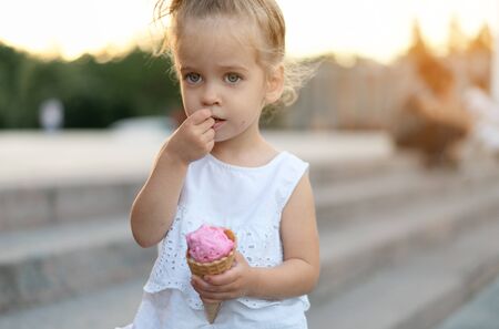 Little caucasian girl 3 years old eats ice cream closeup portrait. Summertime. Childhood  Child with frozen dessert in hand walking outdoor. Close up portrait european girl witn ice-cream.の写真素材