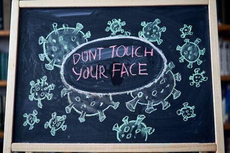 Dont touch your face. Outbreak Warning. written white chalk on blackboard in connection with...