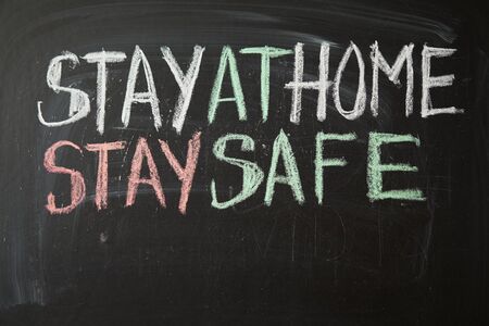 Inscription stay at home stay safe. Outbreak Warning. written white chalk on blackboard in connection with epidemic of coronavirus worldwide. Covid 19 pandemic Text on black backgroundの写真素材