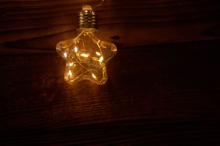 Bright luminous Christmas garlands in the shape of stars lie on a dark wooden background. New year light with copy spaceの写真素材