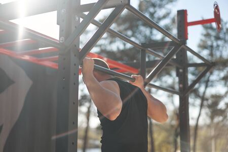 Unrecognizable caucasian men pull-up outdoor workout cross training morning back view Stretching arm...