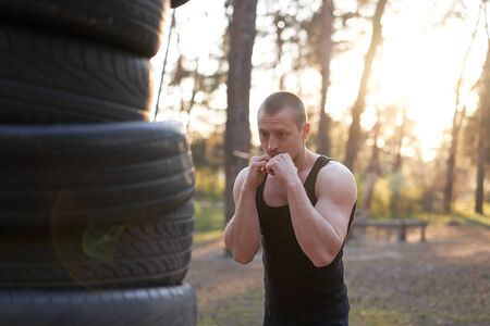 Man fighter training boxing outdoor tire DIY handmade gym in forest fitness workout. Young adult ...