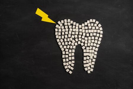 Sugar destroy tooth enamel leads tooth decay  White Sugar cubes shape form tooth brown sugar caries black background Healthcare and medicine Stomatology concept Sweet food destroy teethの写真素材
