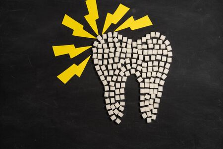 Sugar destroy tooth enamel leads tooth decay  White Sugar cubes shape form tooth brown sugar caries black background Healthcare and medicine Stomatology concept Sweet food destroy teethの写真素材