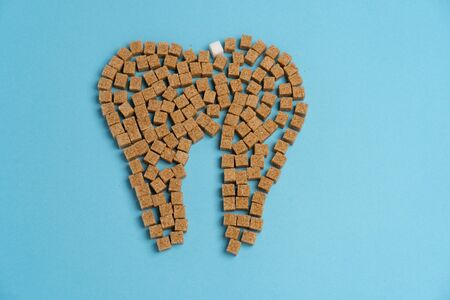 Sugar destroy tooth enamel leads tooth decay  White Sugar cubes shape form tooth brown sugar caries blue background Health care and medicine Stomatology concept Sweet food destroy teethの写真素材