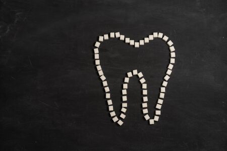 Sugar destroy tooth enamel leads tooth decay  White Sugar cubes shape form tooth brown sugar caries black background Healthcare and medicine Stomatology concept Sweet food destroy teeth の写真素材