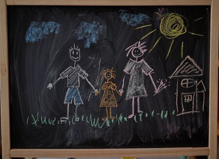 Children multicolored chalk drawing on blackboard Painting on chalkboard  family father mother and daughter holding hands with sun on the sky and sweet home on background の写真素材