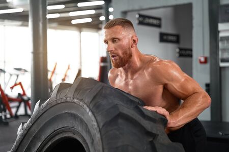Athlete sportive man lift wheel gym cross training push big tire Middle adult handsome sportsman...