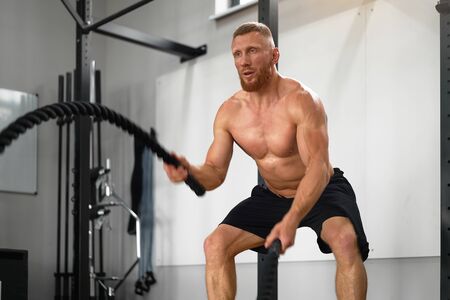 Gym battle rope man stamina training Athlete guy fitness exercising endurance indoor workout....