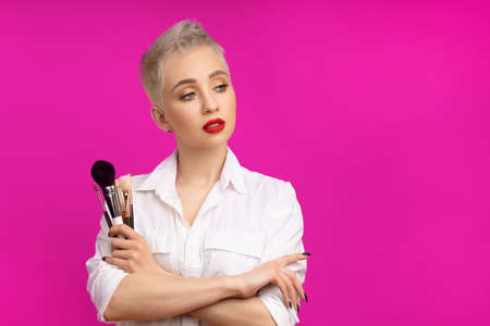 Close up portrait makeup artist. Make up courses. Concept of self visage masterclasess. Fashion professional. Woman hold makeup brushes on the hands. Studio shot on the pinkcolor backgroundの写真素材