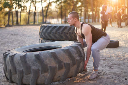 Strong man training workout lifting large tire outdoor DIY gym. Sportive young adult caucasian guy flip big wheel on nature. Handmade equipment sport exercising helthy lifestyle conceptの写真素材
