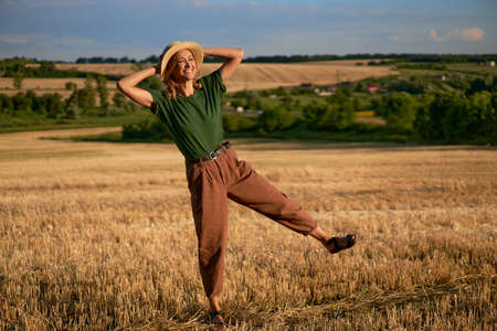 Woman farmer straw hat standing farmland smiling Female agronomist specialist farming agribusiness Happy positive caucasian worker agricultural field Pretty girl denim jeans green t-shirt harvest jumpの写真素材