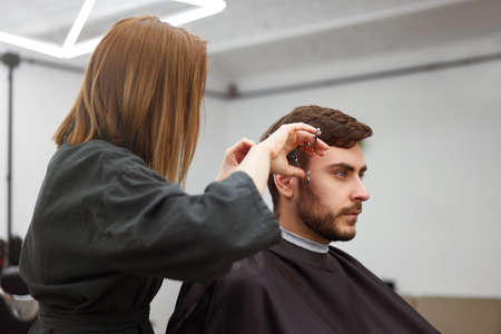 Stylish man sitting barber shop Hairstylist Hairdresser Woman cutting his hair Portrait handsome...