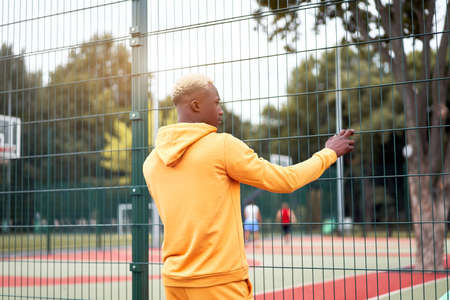 African-american black man yellow hoodie outside Standing back afro model guy walking sport ground summer day Free space Rear viewの素材 [FY310155609528]