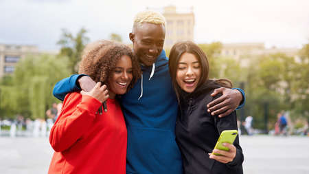Multi ethnic friends outdoor looking smartphone screen. Diverse group people Afro american asian spending time together Multiracial male female student meeting outdoorsの写真素材