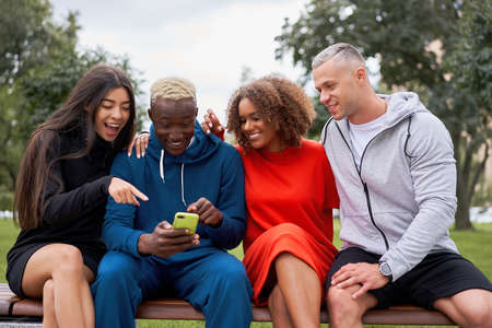 Multi ethnic friends outdoor looking smartphone screen. Diverse group people Afro american asian caucasian spending time together Multiracial male female student meeting outdoorsの写真素材
