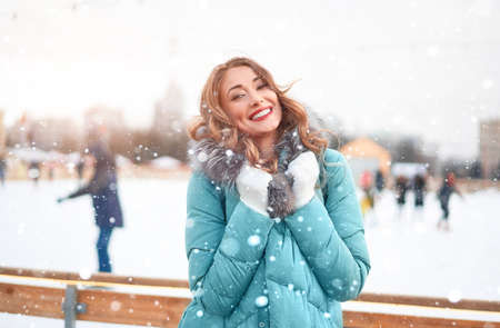 Beautiful lovely middle-aged girl curly hair warm winter jackets white glove stands ice rink background Town Square. Christmas mood lifestyle Happy holiday woman walk snowy day Winter leisureの写真素材