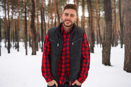 Handsome bearded young caucasian man red checkered shirt standing outdoors winter season forest Attractive stylish european gut walking snowy christmas woodland holiday leisureの写真素材