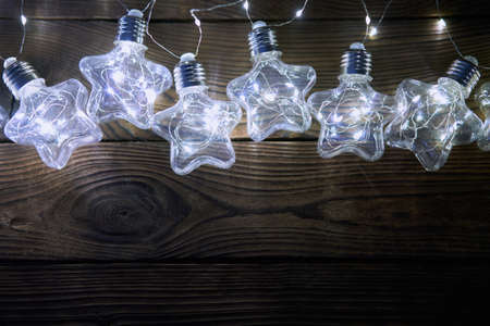 Bright luminous Christmas garlands in the shape of stars lie on a dark wooden background. New year light with copy spaceの写真素材