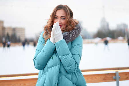 Beautiful lovely middle-aged girl curly hair warm winter jackets white glove stands ice rink background Town Square. Christmas mood lifestyle Happy holiday woman walk snowy day Winter leisureの写真素材