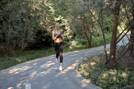 Woman running asphalt road summer park Active sporty caucasian female morning workout Healthy...