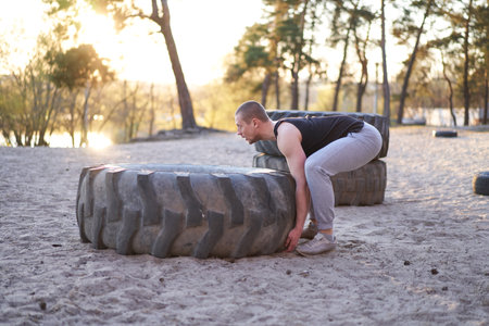 Strong man training workout lifting large tire outdoor DIY gym. Sportive young adult caucasian guy...