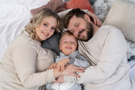 Happy family concept Mother father and little son have fun at home Caucasian family indoors Pregnant mom beard dad and funny little boy lie on the couchの写真素材
