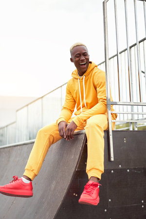 African-american smiling black man yellow hoodie outside Happy emotional afro model guy sitting skate park summer day Free space Positive emotionsの写真素材