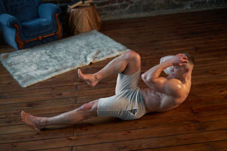 Endurance workout. Strong muscular man pumps abdominal muscles at home interior Caucasian athlete do...