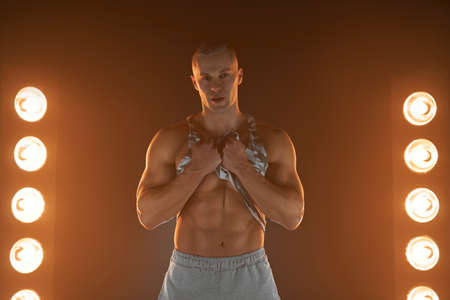 Active lifestyle concept. Professional bodybuilder picks up a t-shirt showing abs muscle and looking...