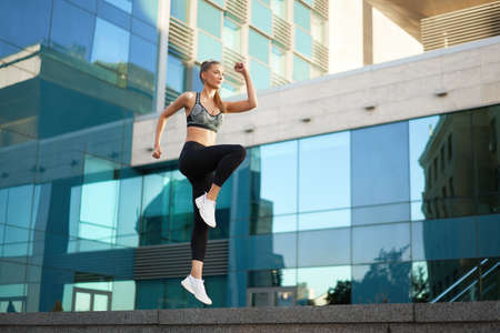 Woman with fit body jumping and running against urban city background. Female model in sportswear...