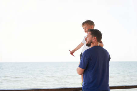 Father son together outside showing finger sea horizon back Man child spending time vacation enjoying summer Family with one child. Caucasian person beachの写真素材
