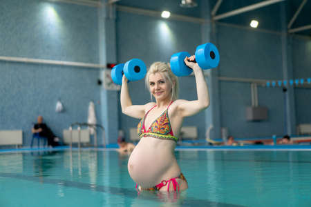 Pregnant woman standing in water with dumbbells indoors swiming pool Active pregnancy Sport and fitnes concept Helthy lifestyleの写真素材