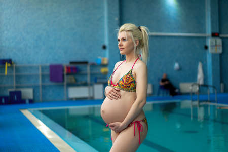 Pregnant woman standing indoors swiming pool hugg big tummy Active pregnancy Sport and fitnes concept Helthy lifestyleの写真素材