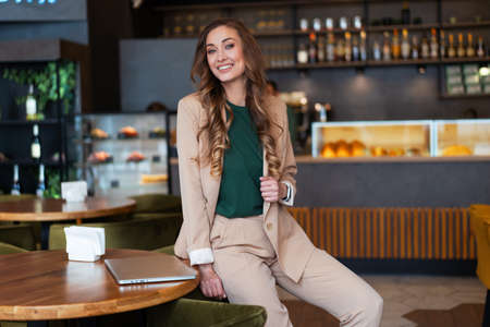 Business Woman Restaurant Owner With Laptop In Hands Dressed Elegant Pantsuit Sitting On Table In Restaurant With Bar Counter Background Caucasian Female Business Person Indoorの写真素材