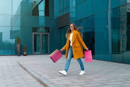 Business Woman With Shopping Bags Dressed Yellow Coat Walking Outdoors Corporative Building Background Caucasian Female Business Person Office Building Stylish Businesswoman Season Sale full lengthの写真素材