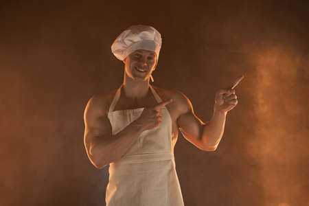 New normal concept. Portrait of muscular chef wearing protective medical mask white apron and cheef hat, standing on smoky background and lamp light male housewife. husband in kitchen. brutal butcher.の写真素材