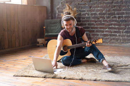 Caucasian young adult learning guitar online music class with distant teacher computer mobile device. Handsome hipster man teaching music through laptop, distance education learning conceptの写真素材