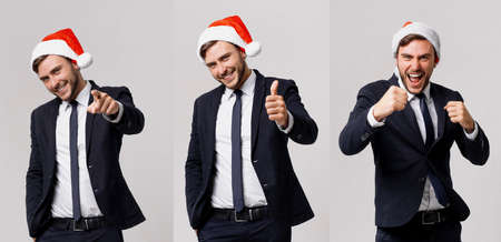 Handsome caucasian guy business suit and Santa hats white background studio smilie showing thumbs up. Business person Christmas mood Holiday mood Businessman positive emotionsの写真素材