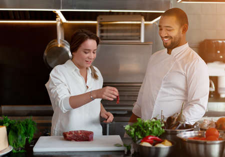 Handsome young African chef is cooking together with Caucasian girlfriend in the kitchen A cook teaches a girl how to cook. Man and woman cooking in professional kitchen. interracial relationshipの写真素材