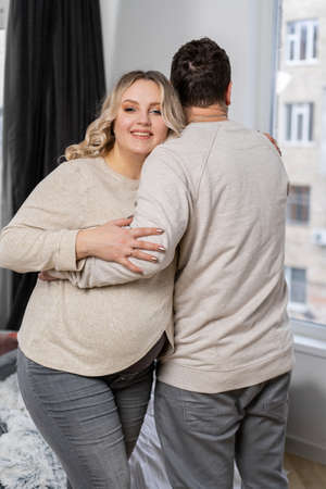 Happy family concept. Husband hug belly pregnant wife standing indoor living room near sofa Caucasian man and woman pregnancy and new life concept. Love and careの写真素材