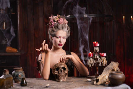 Portrait fortune teller woman reading future on magical scull. Magic and divination. Young beautiful enchanted female witch sitting on the table waiting your desire. Scary Halloween atmosphereの写真素材