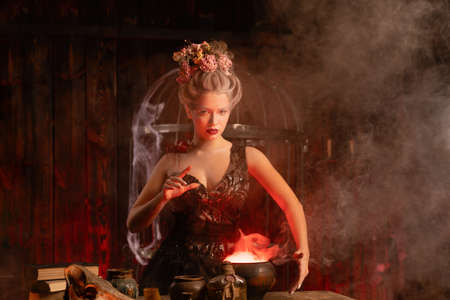 Halloween Witch with cauldron. Beautiful young woman conjuring, making witchcraft. Standing spooky dark magic dungeon dark room. Enchantress prepare love potion use magiÑ spellの写真素材