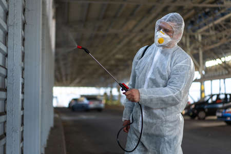 Worker wearing protective suit disinfection gear disinfect surface public place parking. Side view...